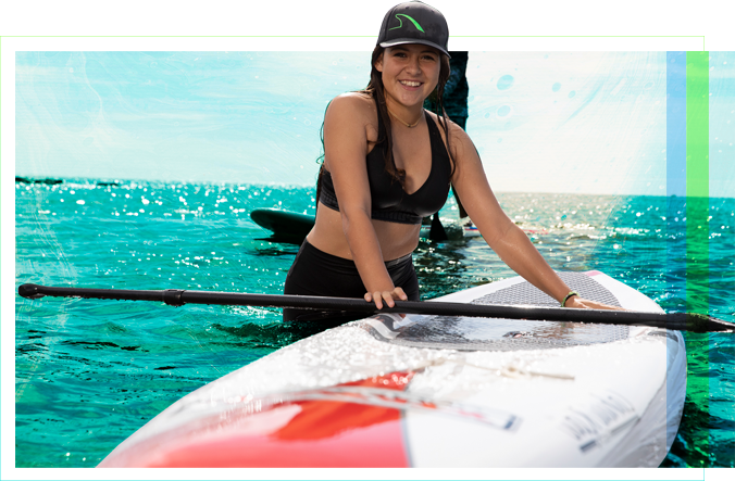 A female student standing in the water next to a paddleboard with the oar laid across it.